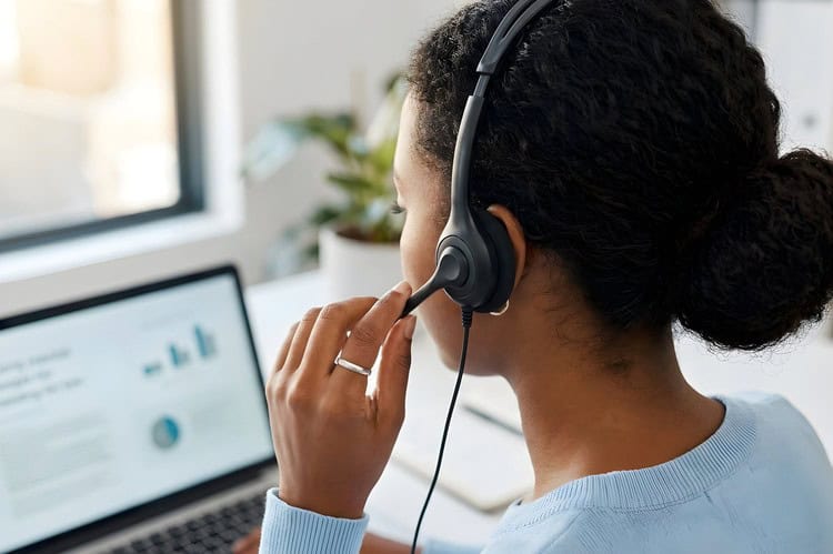 Customer service agent adjusting her headset microphone while looking at charts on her laptop.