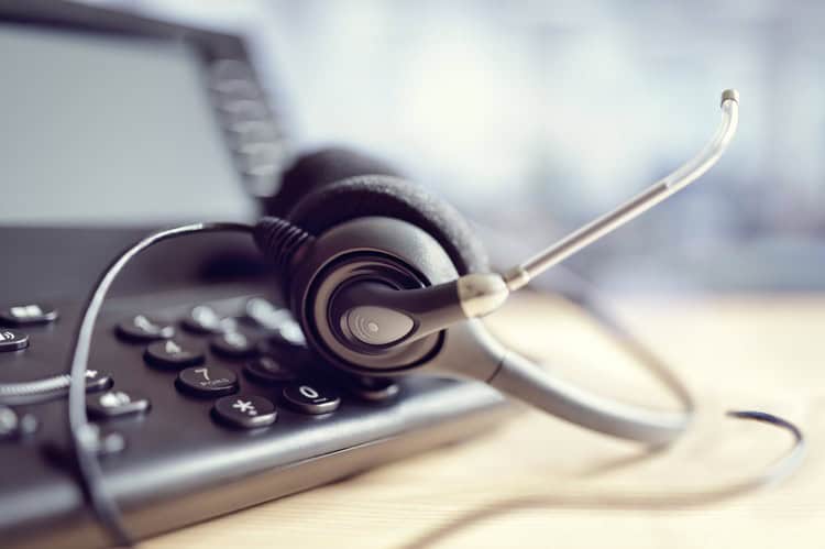 Hand lifting the handset of a black office desk phone with a numeric keypad.