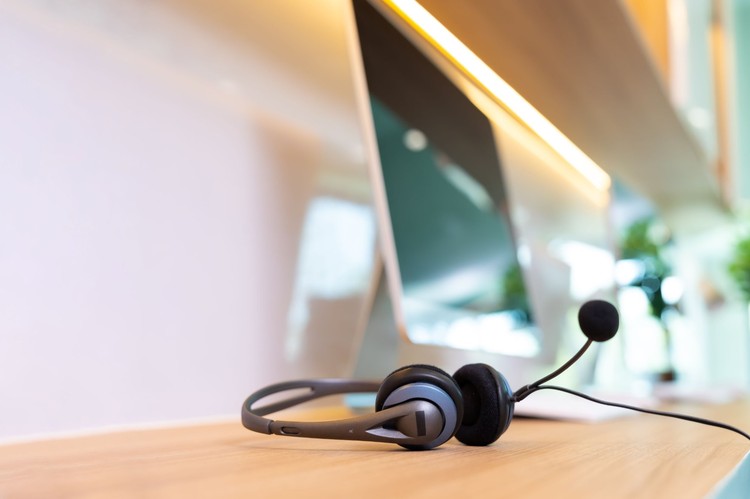 Call centre headset with a microphone resting on a wooden desk in front of a computer monitor.